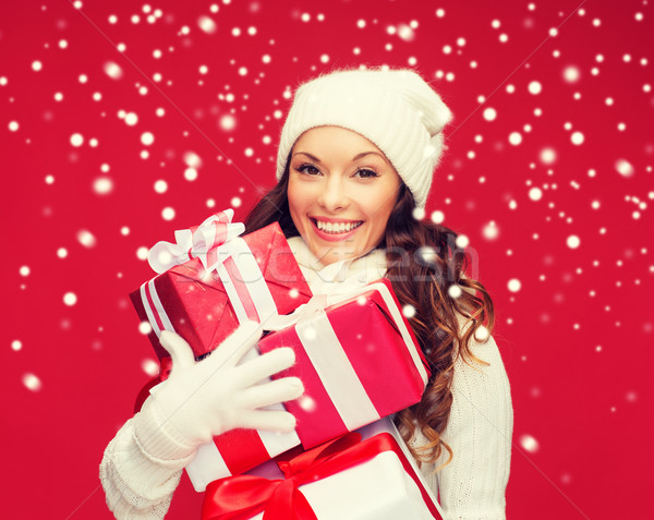 concept - smiling woman in sweater and hat with many gift boxes