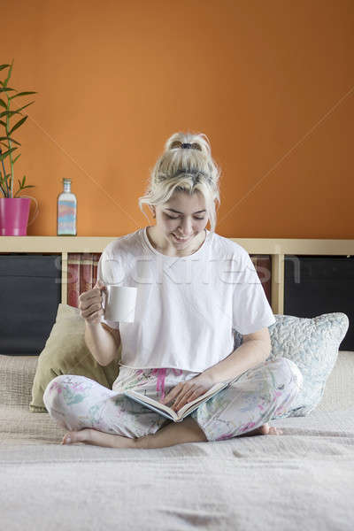Young beautiful blonde-haired female is sitting on bed with a cu Stock photo © 2Design