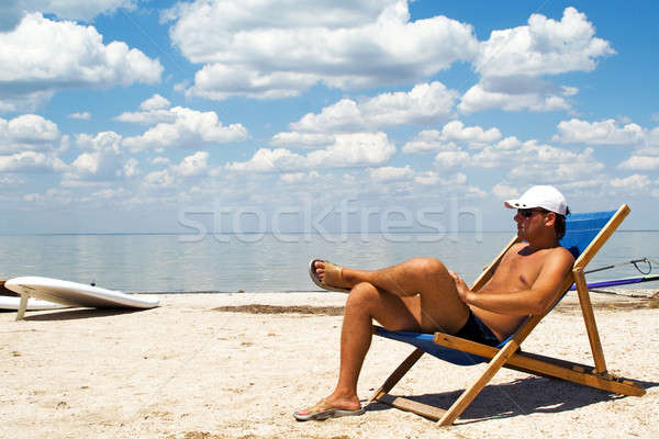 Young man on a chair on a beach against a gulf and clouds Stock photo © acidgrey