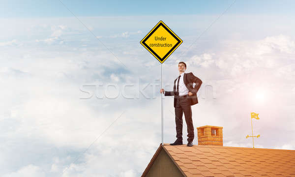 Young businessman on house brick roof holding yellow signboard. Mixed media Stock photo © adam121