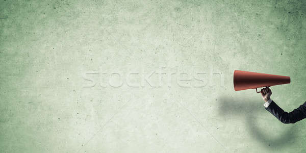 Stock photo: Hand of businesswoman holding red paper trumpet against concrete background