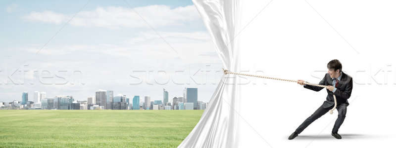 Stock photo: Young man opening white curtain and presenting modern city landscape