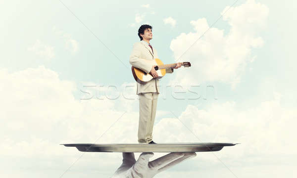 Businessman on metal tray playing acoustic guitar against blue s Stock photo © adam121