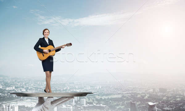 Attractive businesswoman on metal tray playing acoustic guitar against cityscape background Stock photo © adam121