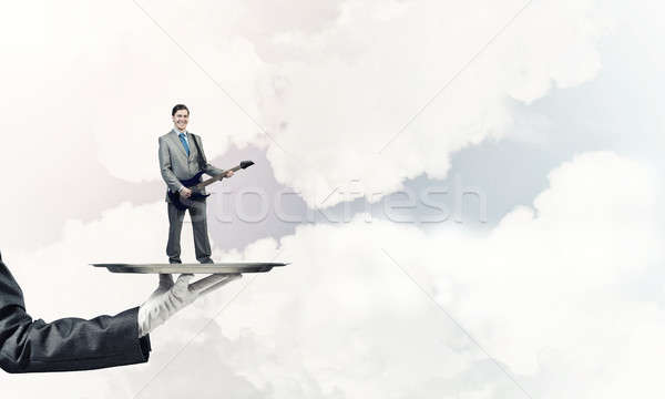 Businessman on metal tray playing electric guitar against blue s Stock photo © adam121