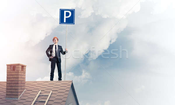 Stock photo: Young businessman with parking sign standing on brick roof. Mixe