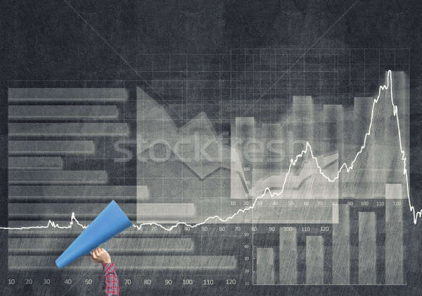 Stock photo: Hand of woman holding blue paper trumpet against graphs backgrou