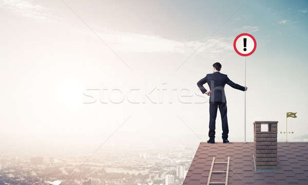 Businessman on house top showing sign with exclamation mark. Mix Stock photo © adam121
