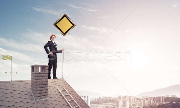 Young businessman on house brick roof holding yellow signboard a Stock photo © adam121