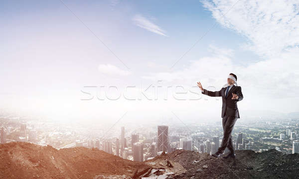 Young businessman in blindfold walking carefully and cityscape at background Stock photo © adam121