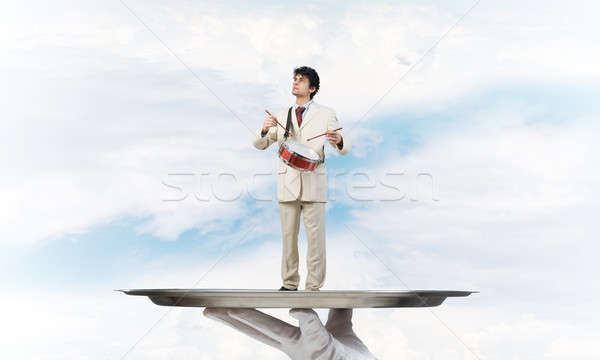 Young businessman on metal tray playing drums against blue sky background Stock photo © adam121