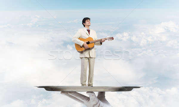 Businessman on metal tray playing acoustic guitar against blue sky background Stock photo © adam121