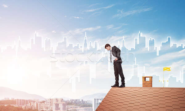 Businessman looking down from roof and modern cityscape at background. Mixed media Stock photo © adam121