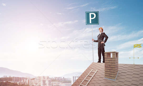 Stock photo: Young businessman with parking sign standing on brick roof. Mixed media