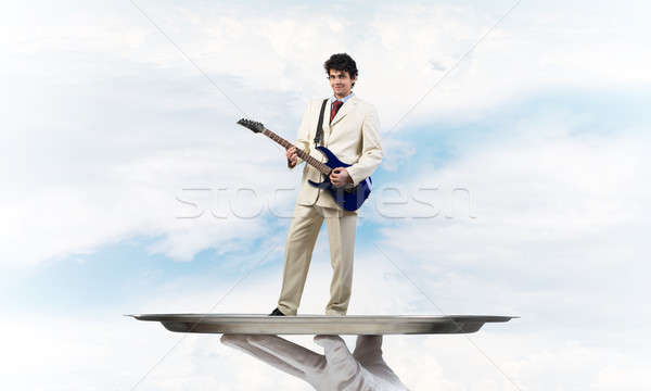 Businessman on metal tray playing electric guitar against blue sky background Stock photo © adam121