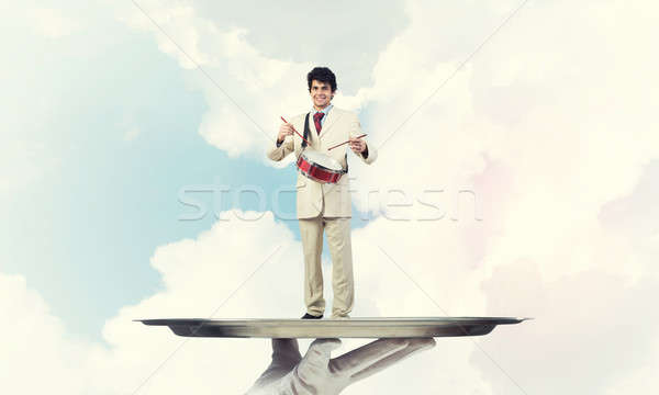 Young businessman on metal tray playing drums against blue sky b Stock photo © adam121