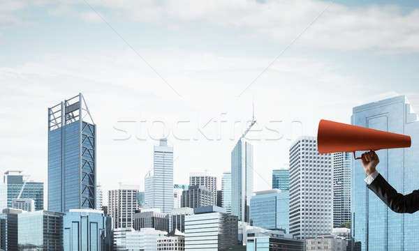 Hand of businesswoman holding red paper trumpet against cityscape background Stock photo © adam121