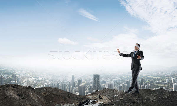 Stock photo: Young businessman in blindfold walking carefully and cityscape at background