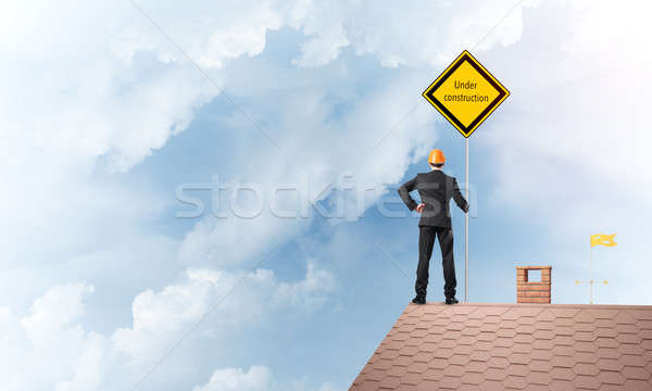 Young businessman on house brick roof holding yellow signboard. Mixed media Stock photo © adam121