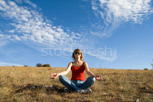 She sits on the ground under a blue sky with clouds and meditate Stock photo © All32