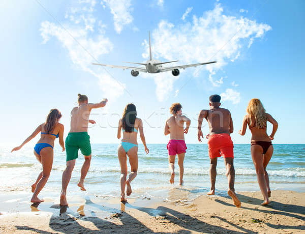 Stock photo: Group of friends run to the sea with an aircraft in the sky. Concept of travel and summer