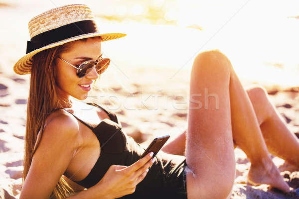 Beautiful girl sends a message with her smartphone at the beach Stock photo © alphaspirit