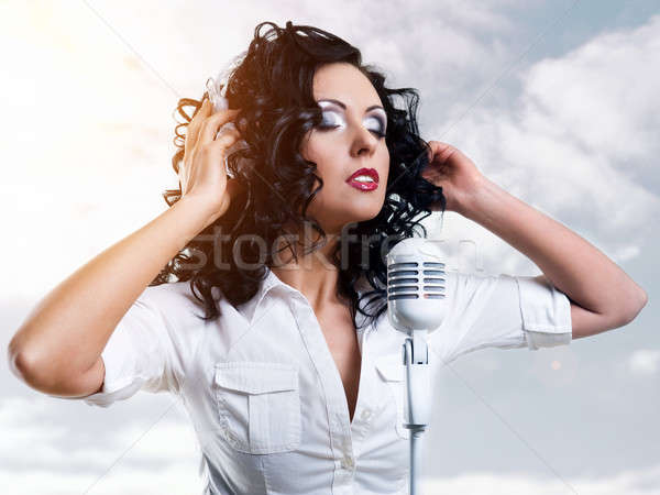 Beautiful young woman with headphones and microphone over clouds Stock photo © amok