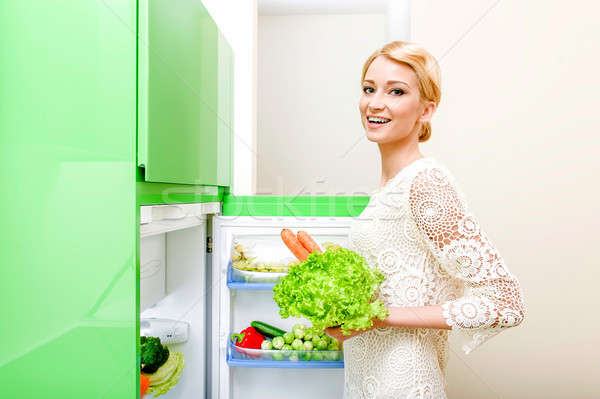 Smiling young woman taking vegetables out of fridge Stock photo © amok
