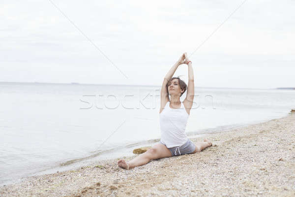 Beautiful girl practicing yoga on the beach near the sea. Sits on a twine, does a stretching. Stock photo © andreonegin