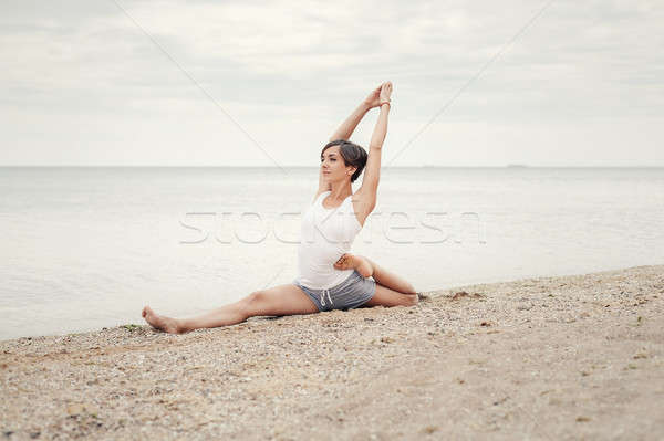 Beautiful girl practicing yoga on the beach near the sea. Sits on a twine, does a stretching. Stock photo © andreonegin