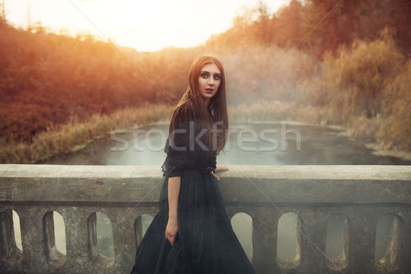 Young attractive Witch walking on the bridge in heavy black smoke. Stock photo © andreonegin