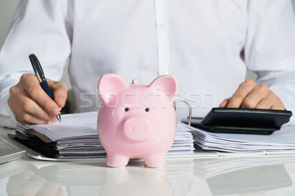 Businessman Calculating Invoice With Piggybank At Desk Stock photo © AndreyPopov