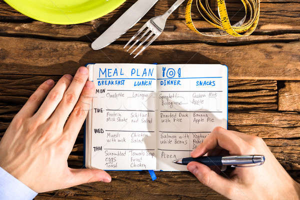 Elevated View Of Human Hand Making Meal Plan On Notebook Stock photo © AndreyPopov