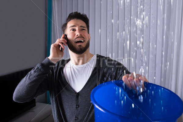 Man Collecting Water In Bucket While Calling Plumber Stock photo © AndreyPopov