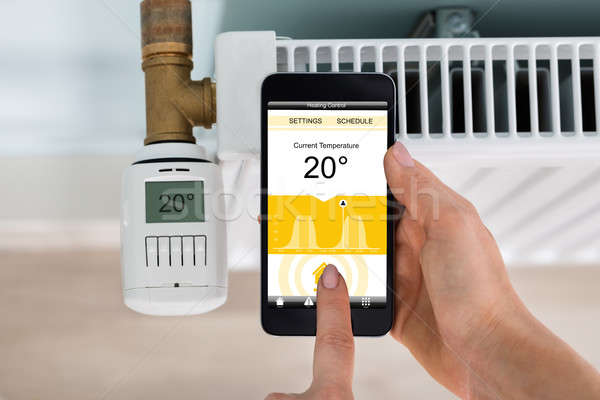 Person Setting Temperature Of Thermostat Using Mobilephone Stock photo © AndreyPopov