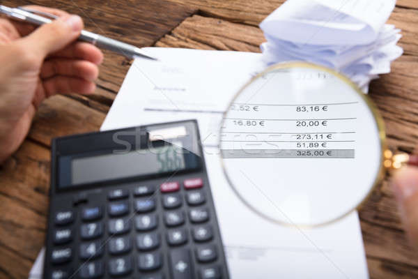 Businessman Examining Invoice With Magnifying Glass At Table Stock photo © AndreyPopov