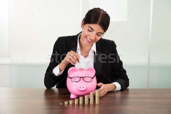 Stock photo: Businesswoman Inserting Coin In Piggybank
