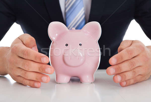 Businessman Protecting Piggybank With Cupped Hands On Desk Stock photo © AndreyPopov