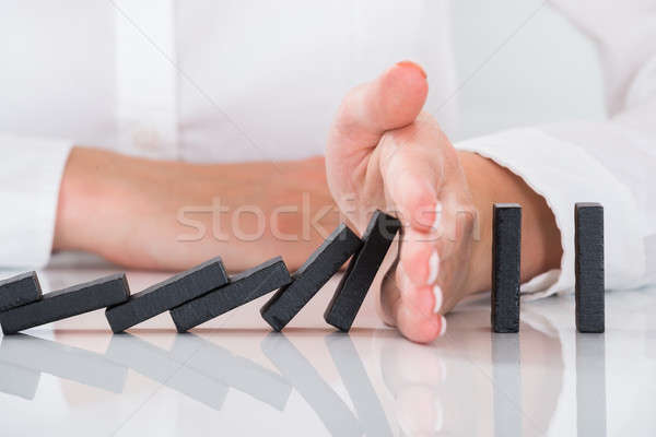 Person's Hand Stopping Dominos Falling On Desk Stock photo © AndreyPopov