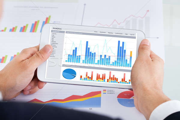Businessman Comparing Graphs On Digital Tablet At Office Desk Stock photo © AndreyPopov