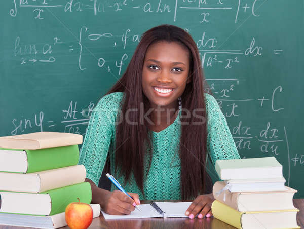 Stock photo: Confident female teacher writing in book at classroom desk