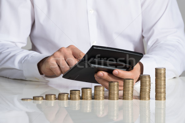 Stock photo: Businessman Using Calculator With Stacked Coins Arranged At Desk