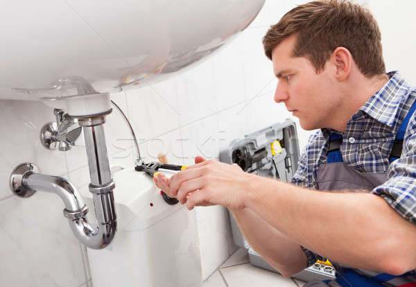 Stock photo: Young plumber fixing a sink in bathroom
