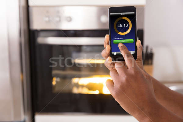 Stock photo: Woman Operating Oven Appliance With Mobile Phone App