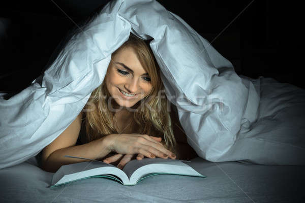 Woman Under Bedding Reading Book Stock photo © AndreyPopov