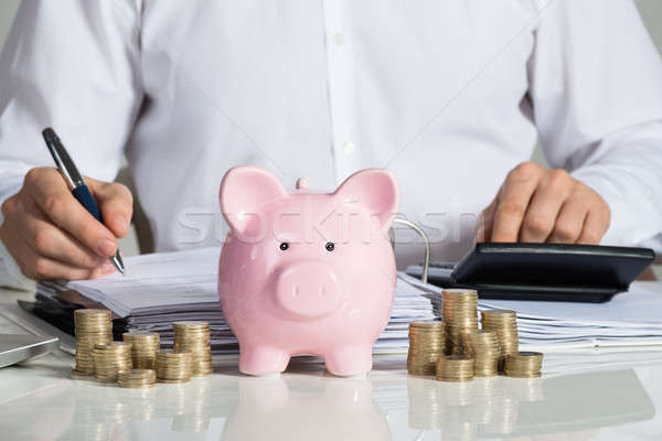 Businessman Calculating Invoice With Piggybank And Coins At Desk Stock photo © AndreyPopov