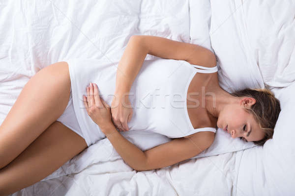 Stock photo: Woman Sleeping On Bed Having Stomach Ache