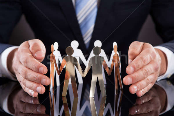 Businessman's Hands Protecting Team Of Paper People On Desk Stock photo © AndreyPopov