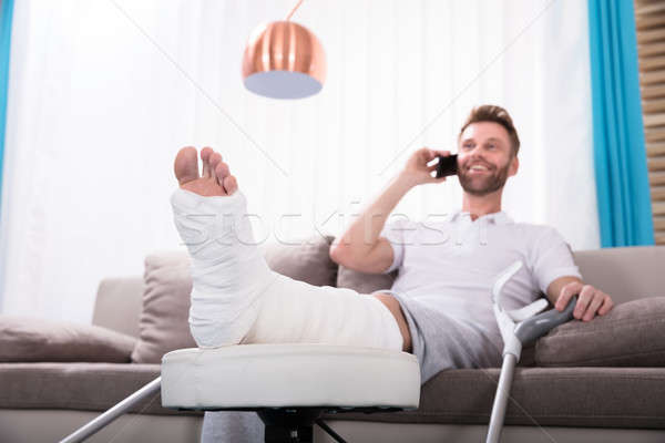 Heureux jeune homme jambe cassée parler smartphone séance Photo stock © AndreyPopov