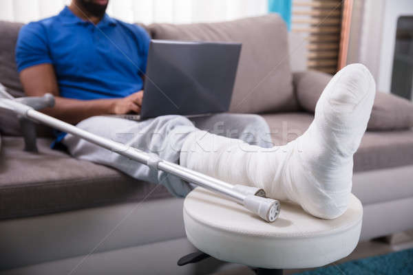 Om picior rupt folosind laptop şedinţei canapea zâmbet Imagine de stoc © AndreyPopov